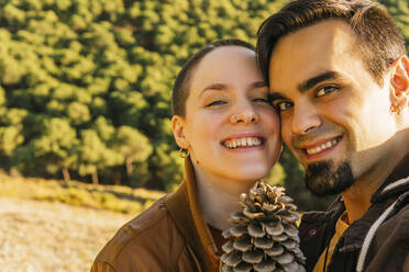 Smiling couple with pine cone on mountain - MGRF00514