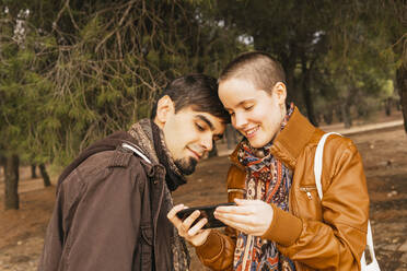 Freundin benutzt Smartphone mit Freund im Wald - MGRF00537