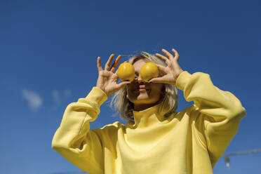 Mittlere erwachsene Frau, die an einem sonnigen Tag ihre Augen mit einer Zitrone bedeckt - LLUF00167