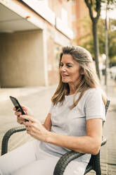 Smiling mature woman surfing net through mobile phone at sidewalk cafe - GRCF01010