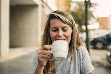 Lächelnde blonde Frau genießt Kaffee in einem Straßencafé - GRCF01013