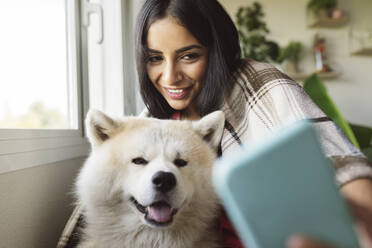 Lächelnde Frau nimmt Selfie mit Hund zu Hause - JCCMF04205