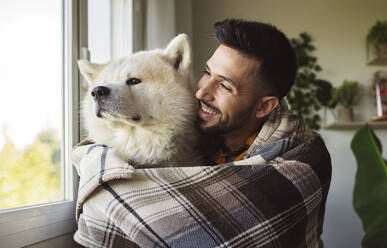 Glücklicher Mann umarmt Akita-Hund am Fenster - JCCMF04209