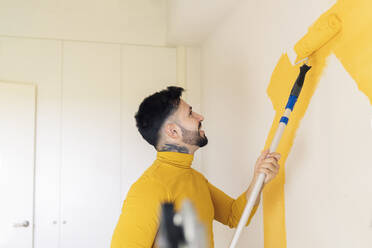 Mid adult man painting wall with paint roller at home - JCCMF04224