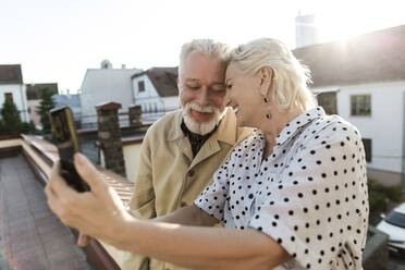 Lächelnde Frau nimmt Selfie mit Mann durch Smartphone auf Terrasse - LLUF00202