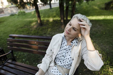 Ältere Frau mit Kopf in der Hand auf einer Bank sitzend - LLUF00209