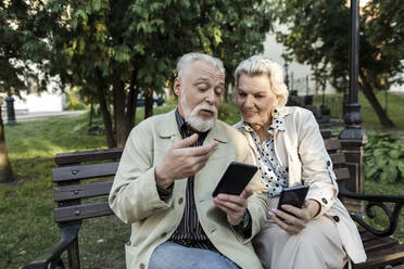 Couple using smart phones while sitting on bench - LLUF00210