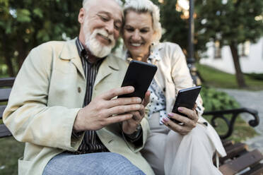 Paar benutzt Smartphone auf einer Bank sitzend - LLUF00212