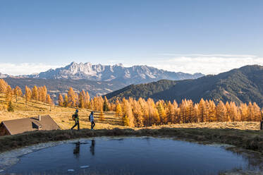Zwei Wanderer gehen im Herbst an einem kleinen Teich in den Ennstaler Alpen vorbei - HHF05808
