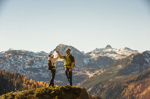 Zwei Wanderer, die sich auf dem Gipfel einer Kante in den Ennstaler Alpen zuprosten - HHF05810