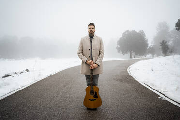 Mann mit Gitarre steht im Winter auf der Straße - RCPF01337