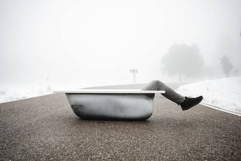 Man resting in bathtub on road during winter - RCPF01351