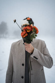 Mann bedeckt Gesicht mit Blumenstrauß im Winter - RCPF01381