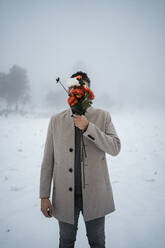 Mature man covering face with bunch of flowers during winter - RCPF01382