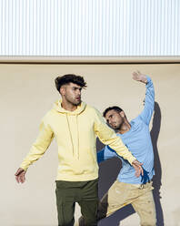 Selbstbewusste männliche Freunde tanzen zusammen vor einer Kulisse an einem sonnigen Tag - RCPF01394
