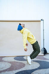 Junger Mann mit geschlossenen Augen balanciert beim Tanzen vor einer Kulisse - RCPF01413