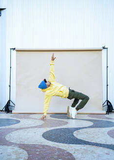 Junger männlicher Darsteller balanciert beim Tanzen auf dem Boden vor einer Kulisse - RCPF01417