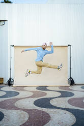 Mid adult man jumping by beige backdrop - RCPF01420