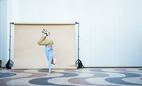 Mid adult man performing handstand on floor by backdrop - RCPF01424