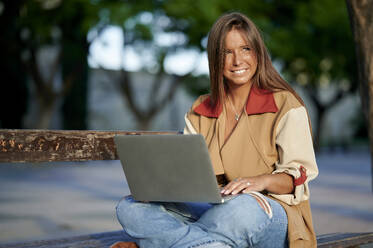 Frau schaut weg, während sie mit Laptop auf einer Bank sitzt - KIJF04175
