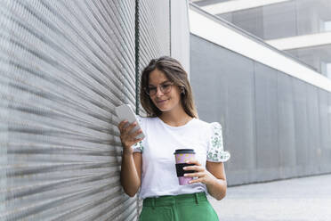 Smiling businesswoman holding coffee cup using smart phone - PNAF02499