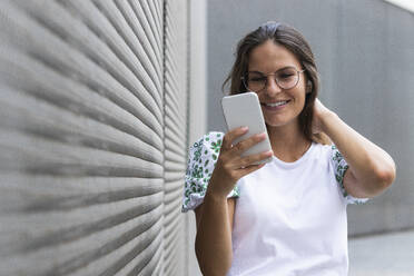 Smiling young businesswoman with hand in hair using mobile phone - PNAF02501