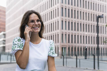 Glückliche junge berufstätige Frau, die mit einem Mobiltelefon spricht - PNAF02512