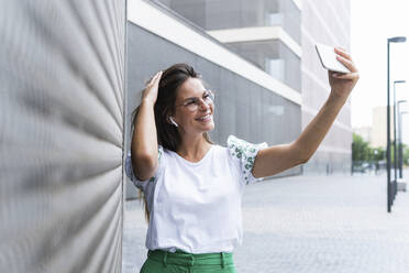 Lächelnde weibliche Fachkraft mit Hand im Haar, die ein Selfie mit ihrem Smartphone macht - PNAF02525