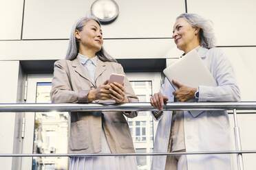 Lächelnde Geschäftsfrauen im Gespräch an einem Geländer - OIPF01321
