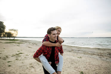Smiling boyfriend giving piggyback ride to girlfriend at beach - LLUF00250