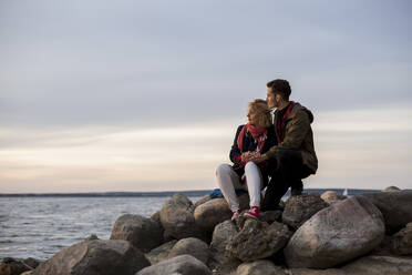 Ehepaar schaut auf das Meer, während es auf einem Felsen sitzt - LLUF00257