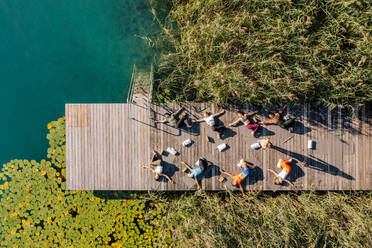 Männer und Frauen üben Yoga auf dem Steg am See während eines sonnigen Tages - DAWF02006