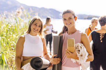 Frauen, die bei einem Yogakurs an einem sonnigen Tag eine Übungsmatte halten - DAWF02014