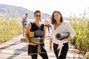 Frauen mit Gymnastikmatten stehen beim Yoga-Kurs auf dem Steg - DAWF02021