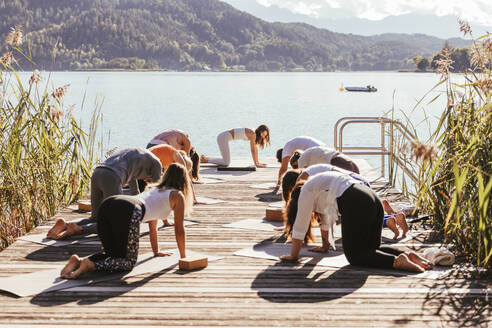 Yogalehrerin unterrichtet Männer und Frauen auf einem Steg am See - DAWF02028