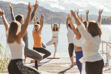 Weibliche Lehrerin unterrichtet Männer und Frauen während einer Yogastunde in Vrikshasana - DAWF02033