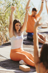 Beautiful woman with arms raised practicing yoga on exercise mat - DAWF02038