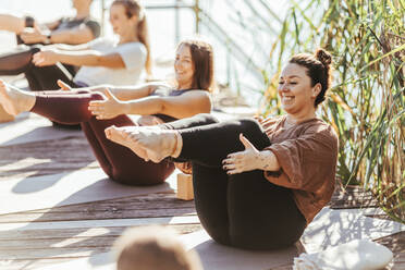 Lächelnde Frauen üben Yoga auf einer Übungsmatte - DAWF02040