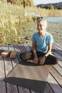 Happy woman looking away while sitting on exercise mat at yoga class - DAWF02053