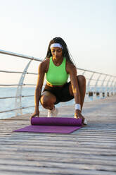 Young female athlete putting yoga mat on broadwalk - OYF00576