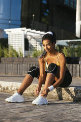 Smiling young athlete tying shoelace while sitting on curb - OYF00597