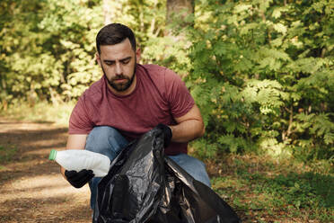 Männlicher Freiwilliger, der eine Plastikflasche in einen Müllsack steckt - VPIF05088