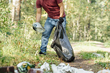 Mittlerer Erwachsener, männlicher Umweltschützer, der eine Plastikflasche in einen Müllsack steckt - VPIF05096