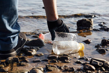 Männlicher Aktivist sammelt Plastikflaschen am Flussufer - VPIF05106