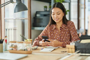 Smiling businesswoman using mobile phone at desk - KIJF04206