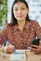 Junge Frau hält Smartphone am Schreibtisch - KIJF04210