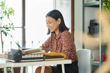 Smiling young businesswoman sitting at desk while working in office - KIJF04211