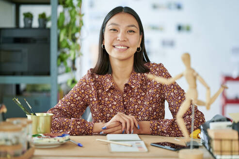 Lächelnde junge Frau, die am Arbeitsplatz sitzt - KIJF04214