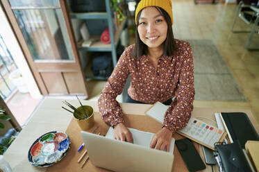 Lächelnde weibliche Fachkraft mit Laptop im Büro sitzend - KIJF04221