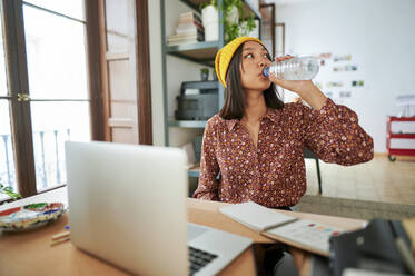 Geschäftsfrau trinkt am Arbeitsplatz Wasser aus einer Flasche - KIJF04222